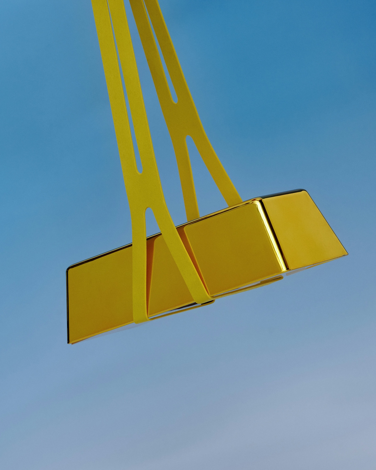 A bright yellow money clip suspended in front of a clear blue sky.